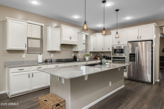 kitchen featuring dark wood-style floors, a kitchen island with sink, a sink, appliances with stainless steel finishes, and white cabinetry