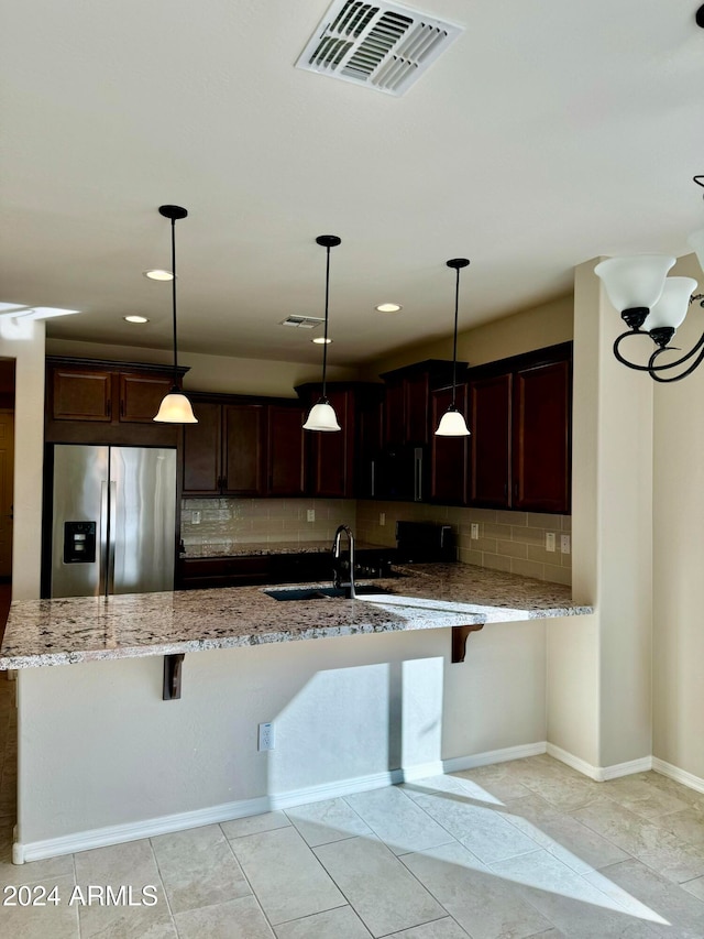 kitchen featuring a breakfast bar area, stainless steel fridge, hanging light fixtures, and light stone counters