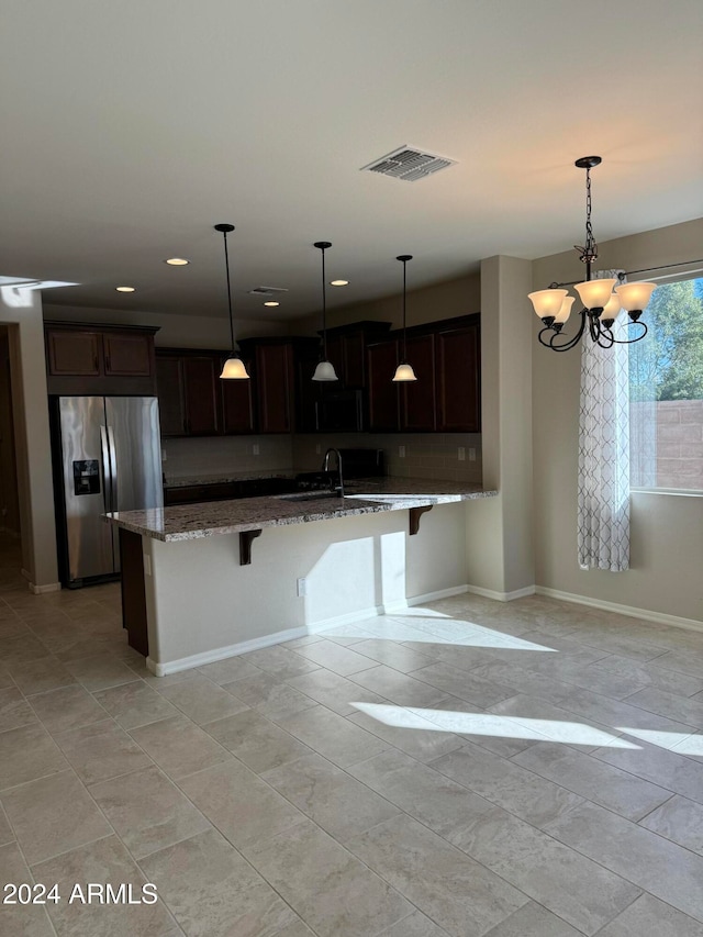 kitchen featuring stainless steel refrigerator with ice dispenser, pendant lighting, a breakfast bar, and light stone countertops