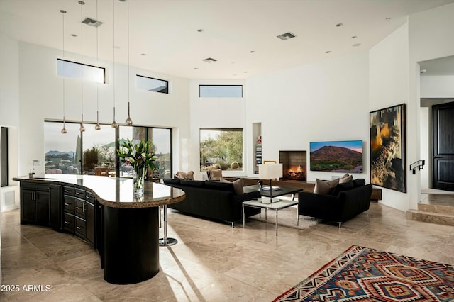 living area with marble finish floor, a lit fireplace, a towering ceiling, and visible vents