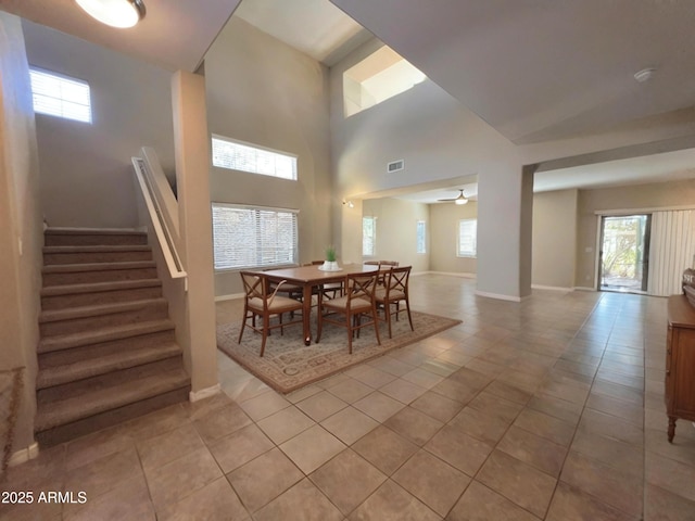 dining area featuring light tile patterned floors, visible vents, baseboards, ceiling fan, and stairs