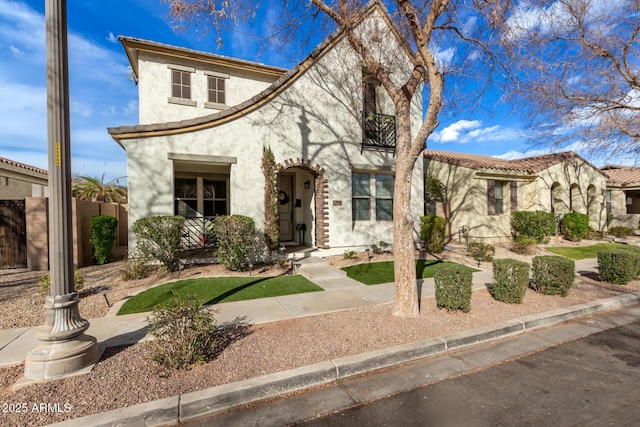 mediterranean / spanish-style house featuring a tile roof, fence, and stucco siding