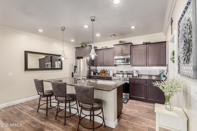 kitchen featuring dark brown cabinetry, stainless steel appliances, a breakfast bar, visible vents, and decorative backsplash