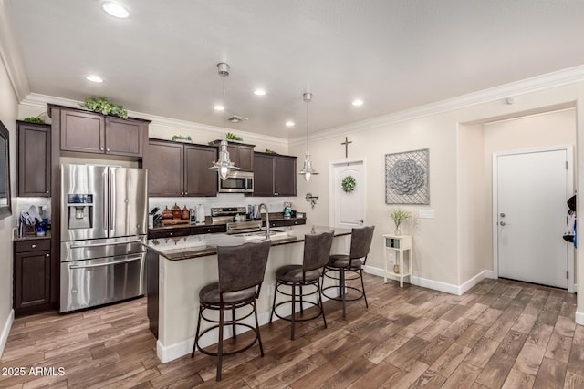 kitchen featuring a breakfast bar area, stainless steel appliances, a sink, backsplash, and a center island with sink