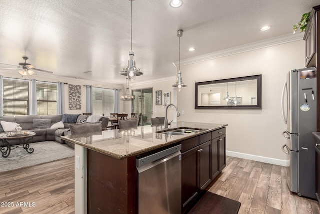 kitchen featuring light stone counters, stainless steel appliances, ornamental molding, a sink, and light wood-type flooring