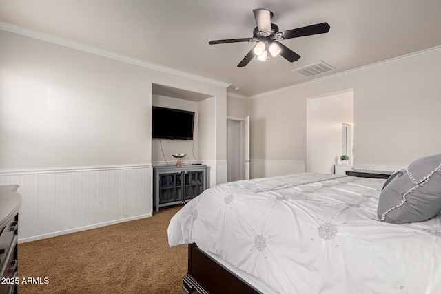 carpeted bedroom with ceiling fan, visible vents, ornamental molding, and wainscoting