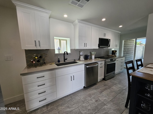 kitchen with backsplash, stainless steel appliances, white cabinets, and a sink