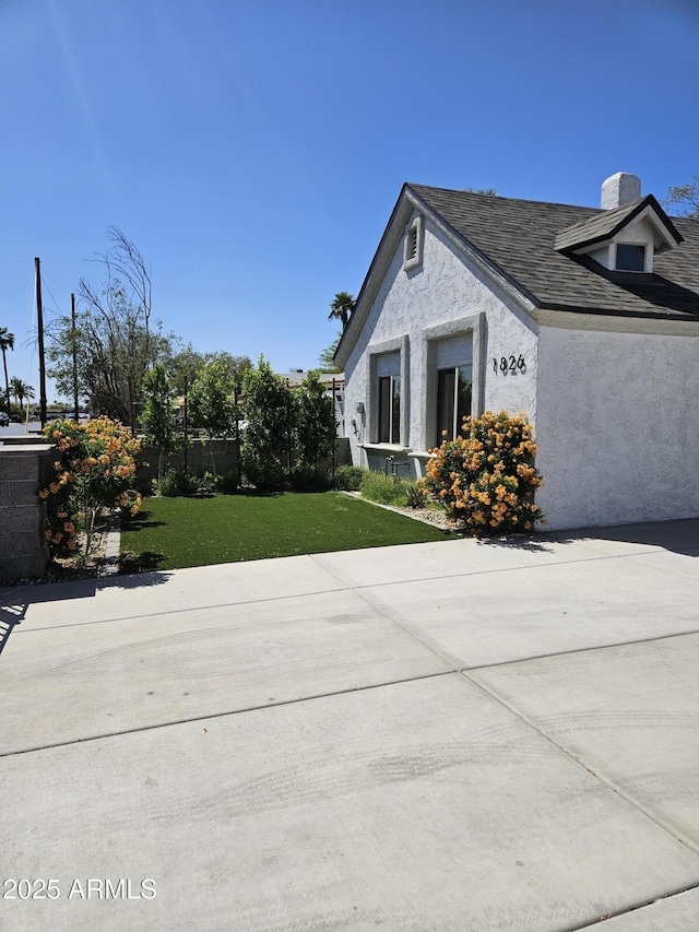 view of property exterior with fence, stucco siding, a chimney, a shingled roof, and a lawn