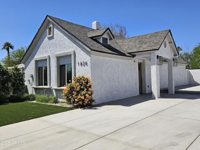 view of front of property featuring a chimney, a shingled roof, a front yard, and stucco siding