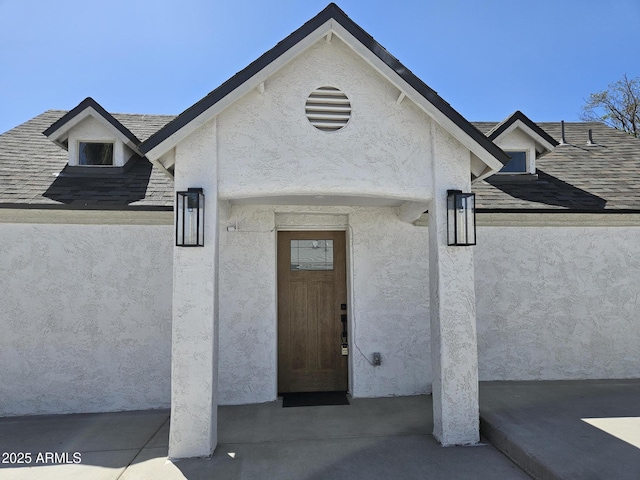 property entrance featuring roof with shingles and stucco siding
