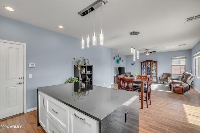 kitchen with light hardwood / wood-style flooring, ceiling fan, decorative light fixtures, a kitchen island, and white cabinetry