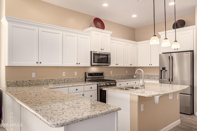 kitchen featuring appliances with stainless steel finishes, decorative light fixtures, sink, white cabinets, and a center island with sink