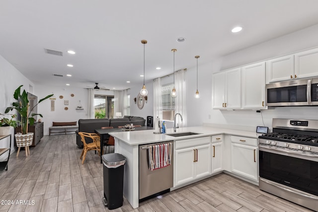 kitchen featuring kitchen peninsula, white cabinets, sink, pendant lighting, and stainless steel appliances