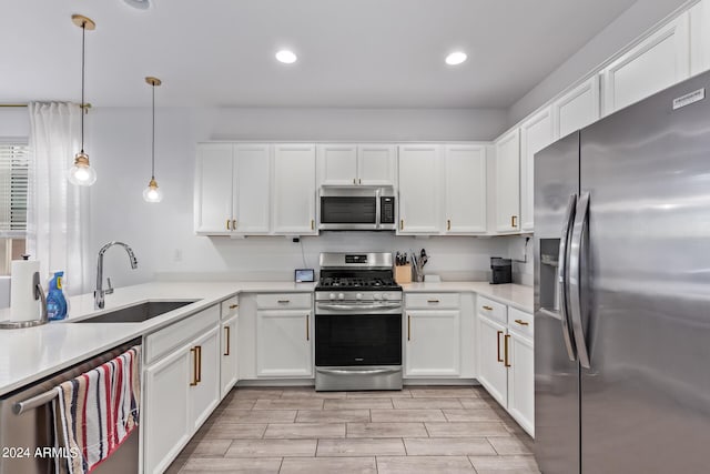 kitchen with sink, stainless steel appliances, pendant lighting, white cabinets, and light hardwood / wood-style flooring