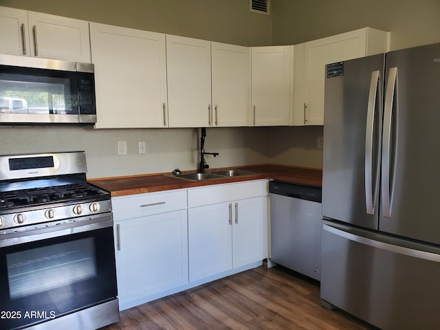 kitchen featuring white cabinets, dark wood finished floors, appliances with stainless steel finishes, wooden counters, and a sink