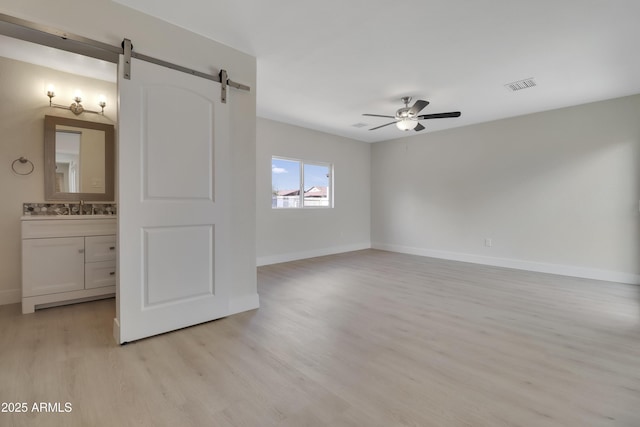 19118 W Fillmore St, Buckeye, AZ 85326 - unfurnished bedroom featuring a barn door, light wood-style floors, a sink, and baseboards