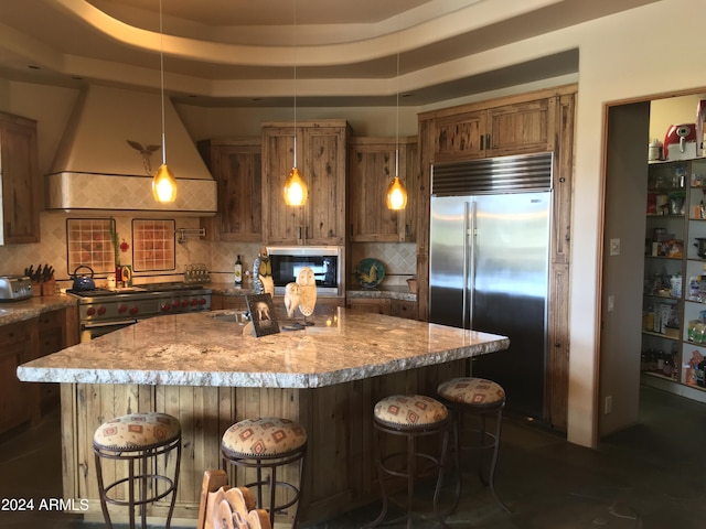 kitchen with backsplash, built in appliances, decorative light fixtures, and a center island with sink