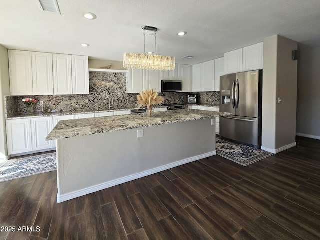 kitchen featuring pendant lighting, white cabinetry, stainless steel refrigerator with ice dispenser, light stone countertops, and an island with sink