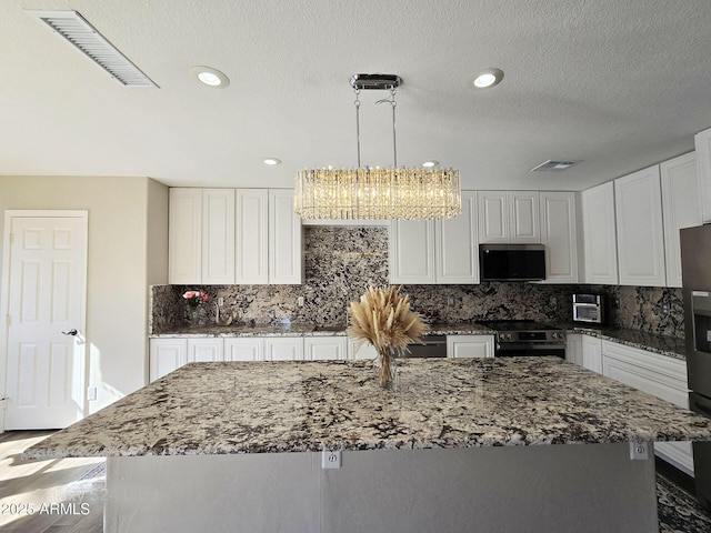 kitchen with white cabinetry, a center island, electric range oven, hanging light fixtures, and dark stone countertops