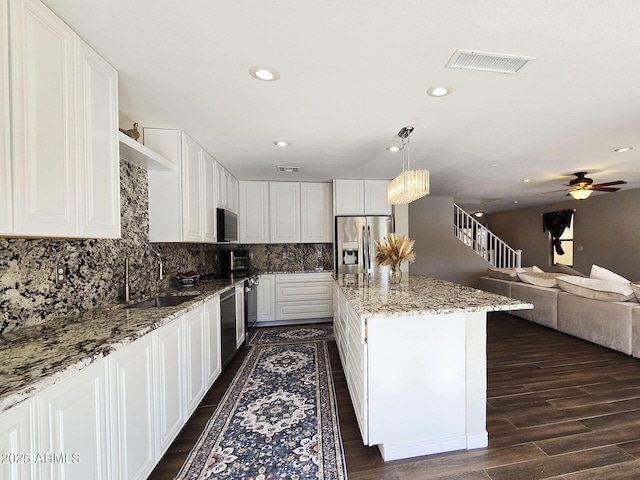 kitchen with sink, hanging light fixtures, stainless steel appliances, light stone countertops, and white cabinets