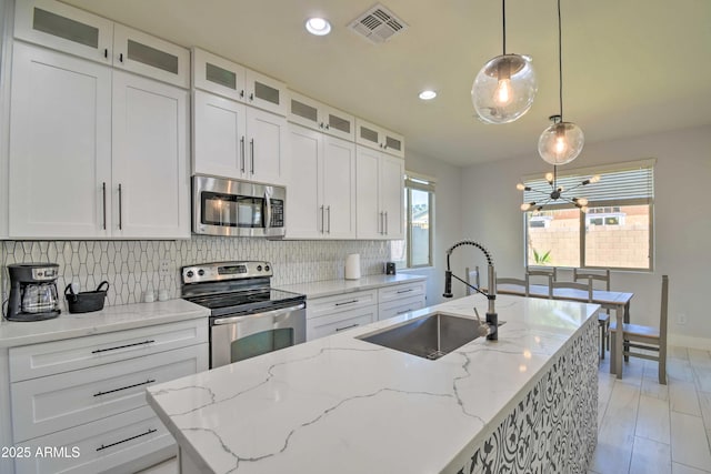 kitchen with sink, pendant lighting, stainless steel appliances, a kitchen island with sink, and white cabinets