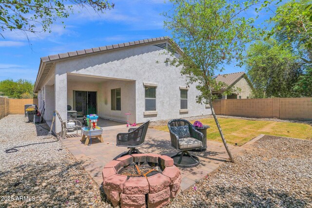back of property with a fenced backyard, stucco siding, an outdoor fire pit, and a patio area