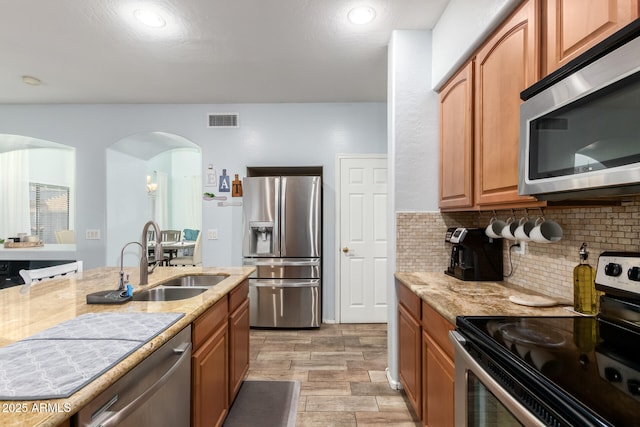 kitchen featuring visible vents, arched walkways, appliances with stainless steel finishes, a sink, and backsplash