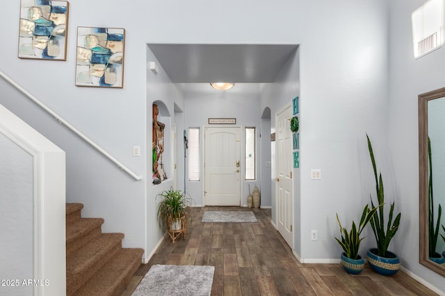 foyer with dark wood-style floors, baseboards, stairs, and arched walkways