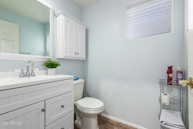 half bathroom featuring toilet, baseboards, and vanity