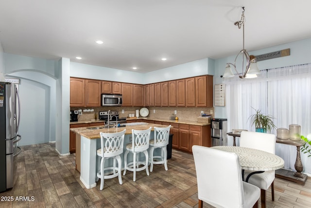 kitchen with dark wood-style floors, appliances with stainless steel finishes, an island with sink, and backsplash