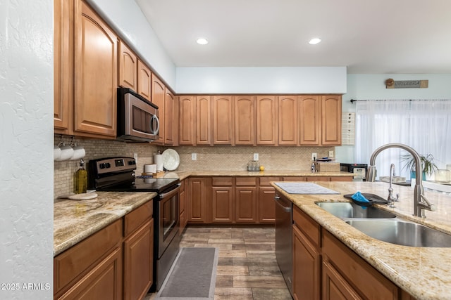 kitchen featuring light stone counters, tasteful backsplash, recessed lighting, appliances with stainless steel finishes, and a sink