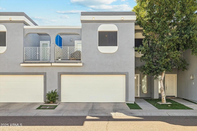 view of property with a garage, a balcony, concrete driveway, and stucco siding