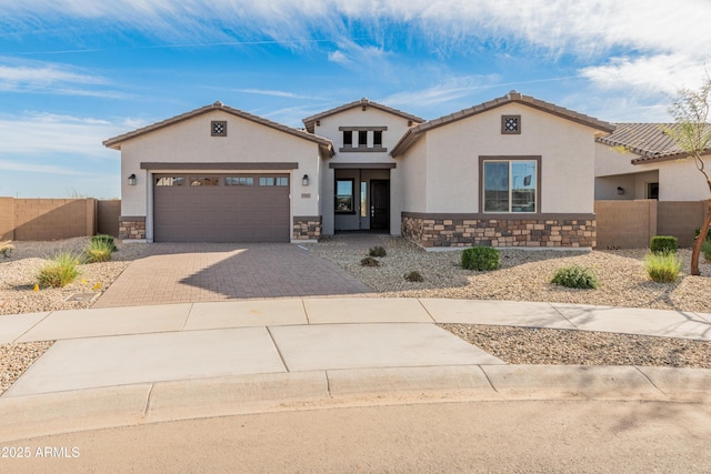 mediterranean / spanish-style house with decorative driveway, stone siding, fence, and a garage