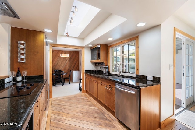 kitchen with a skylight, stainless steel dishwasher, black electric cooktop, sink, and dark stone countertops