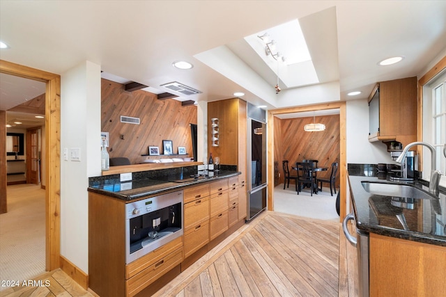 kitchen with a skylight, sink, light carpet, black electric cooktop, and wooden walls