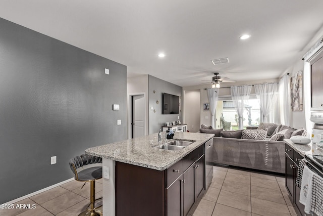 kitchen with sink, dark brown cabinets, light tile patterned floors, stainless steel dishwasher, and an island with sink