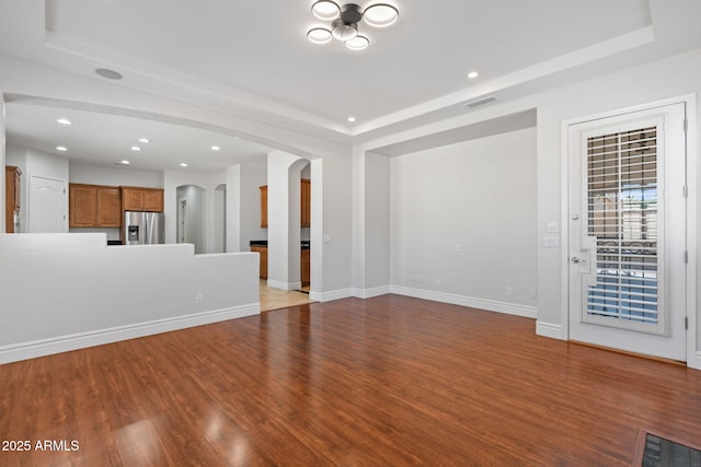 3215 E Constance Way, Phoenix, AZ 85042 - unfurnished living room featuring wood finished floors, arched walkways, a tray ceiling, and recessed lighting