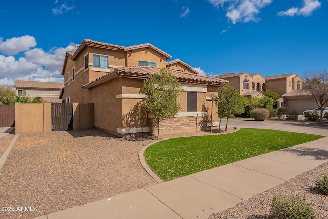 mediterranean / spanish home featuring stucco siding, a gate, fence, a tiled roof, and a front lawn