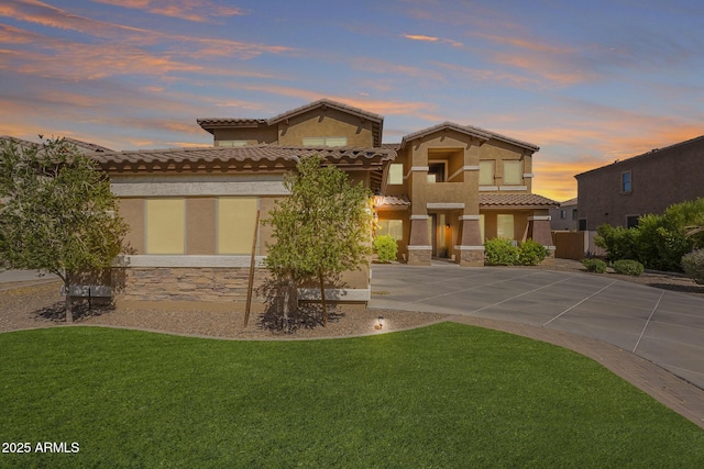 mediterranean / spanish house with driveway, a lawn, stone siding, and stucco siding