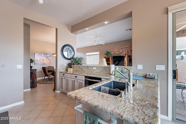 kitchen with light stone countertops, dishwasher, light tile patterned floors, a peninsula, and a sink