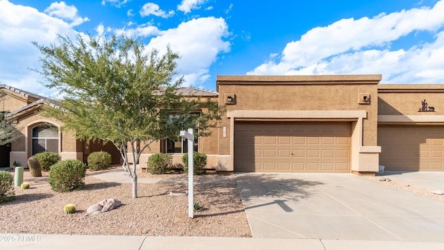 pueblo revival-style home with stucco siding, a garage, and concrete driveway