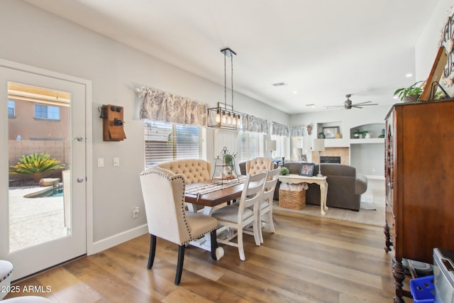 dining space with baseboards, visible vents, a ceiling fan, a tile fireplace, and wood finished floors