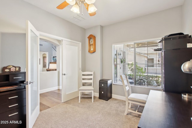 home office featuring arched walkways, light colored carpet, visible vents, ceiling fan, and baseboards