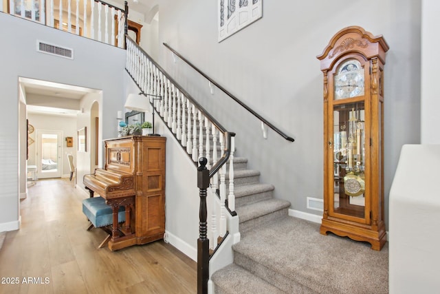 stairway featuring arched walkways, visible vents, a high ceiling, wood finished floors, and baseboards