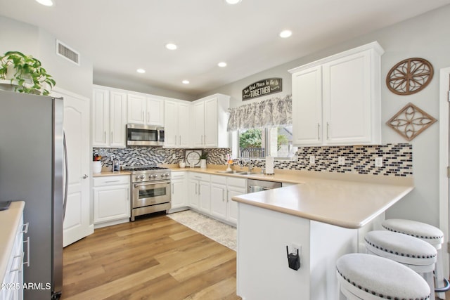 kitchen featuring visible vents, a peninsula, stainless steel appliances, light wood-style floors, and a sink