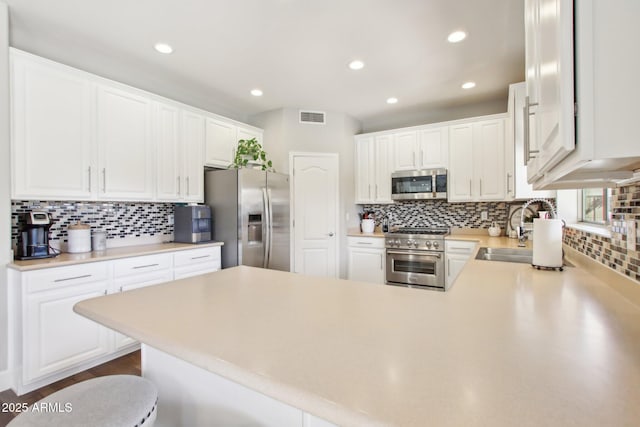 kitchen with visible vents, appliances with stainless steel finishes, a peninsula, white cabinetry, and a sink