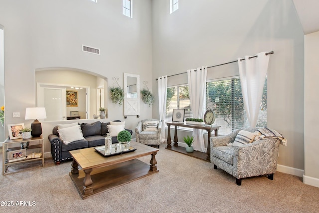 carpeted living area featuring arched walkways, a towering ceiling, visible vents, and baseboards