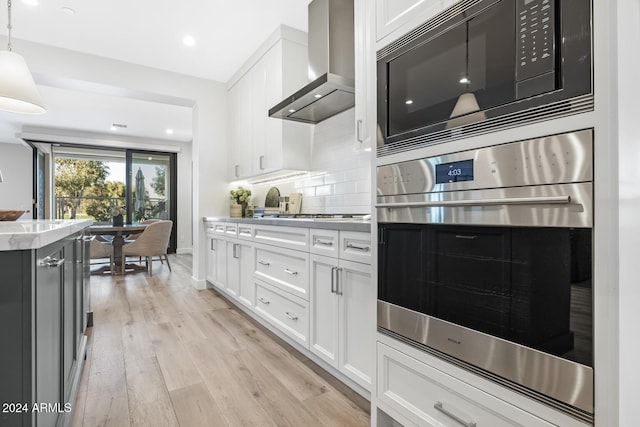 kitchen featuring wall chimney exhaust hood, tasteful backsplash, light hardwood / wood-style floors, white cabinetry, and stainless steel appliances