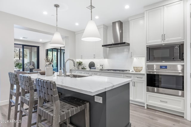 kitchen with white cabinets, wall chimney range hood, sink, hanging light fixtures, and appliances with stainless steel finishes