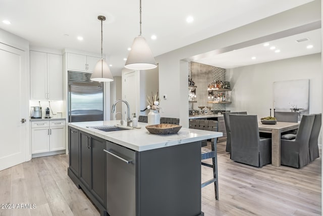 kitchen with sink, hanging light fixtures, built in fridge, a kitchen island with sink, and white cabinets